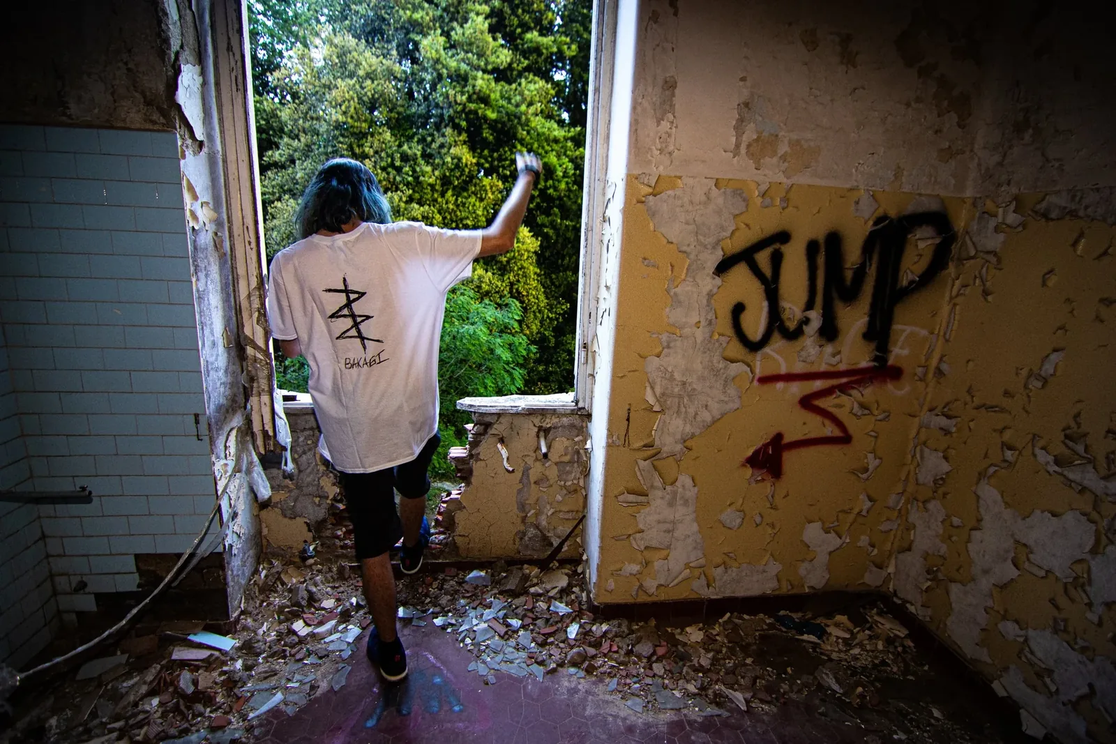 From behind: a man in a white T-shirt climbing through a ruined window, the word Jump painted beside it