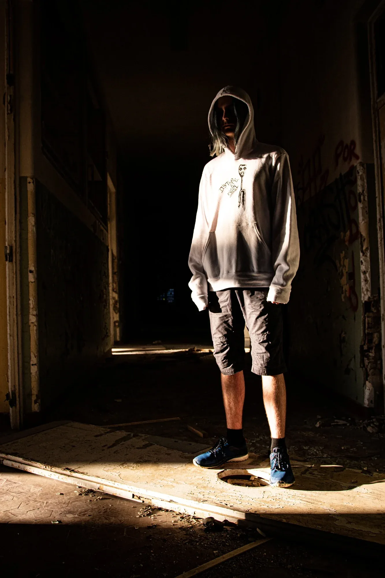 A figure in a white hoodie at the end of a dark, crumbling corridor