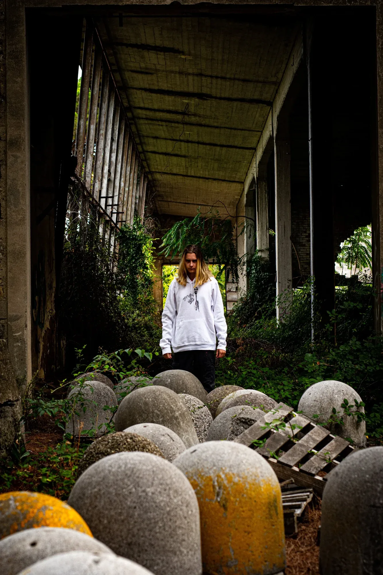 A man in a white hoodie standing among stone bollards under a concrete roof