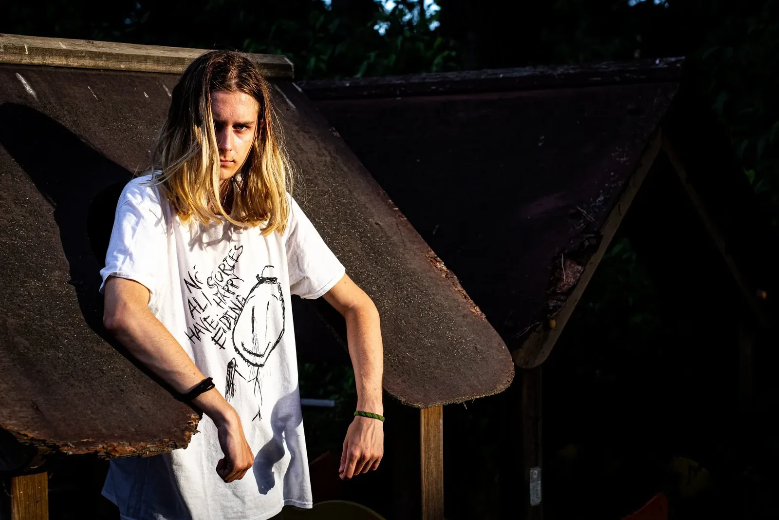A man in a white T-shirt under a broken roof, in deep shade