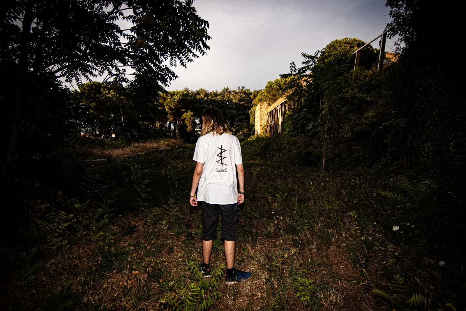 A small figure in a white T-shirt in an overgrown yard