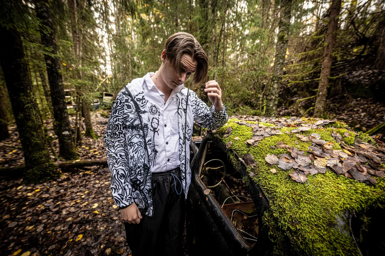 A young man in the Doodled shirt beside a moss-covered car