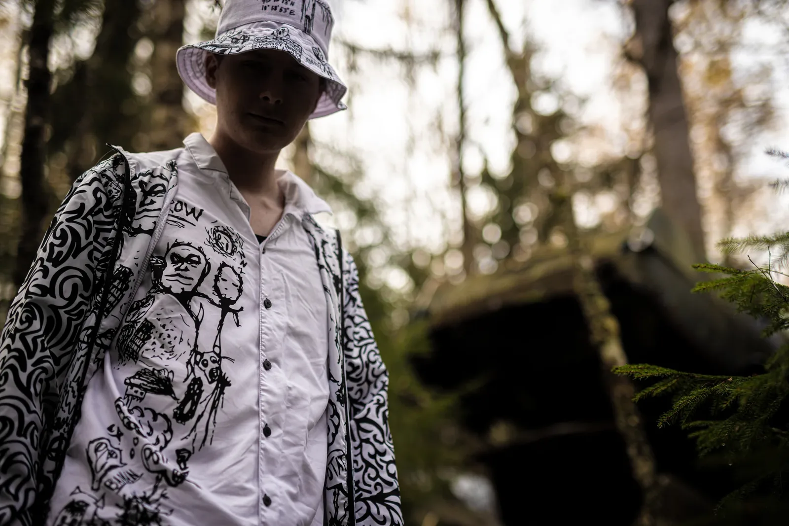 A young man in the OG bucket hat and the Doodled shirt in the forest
